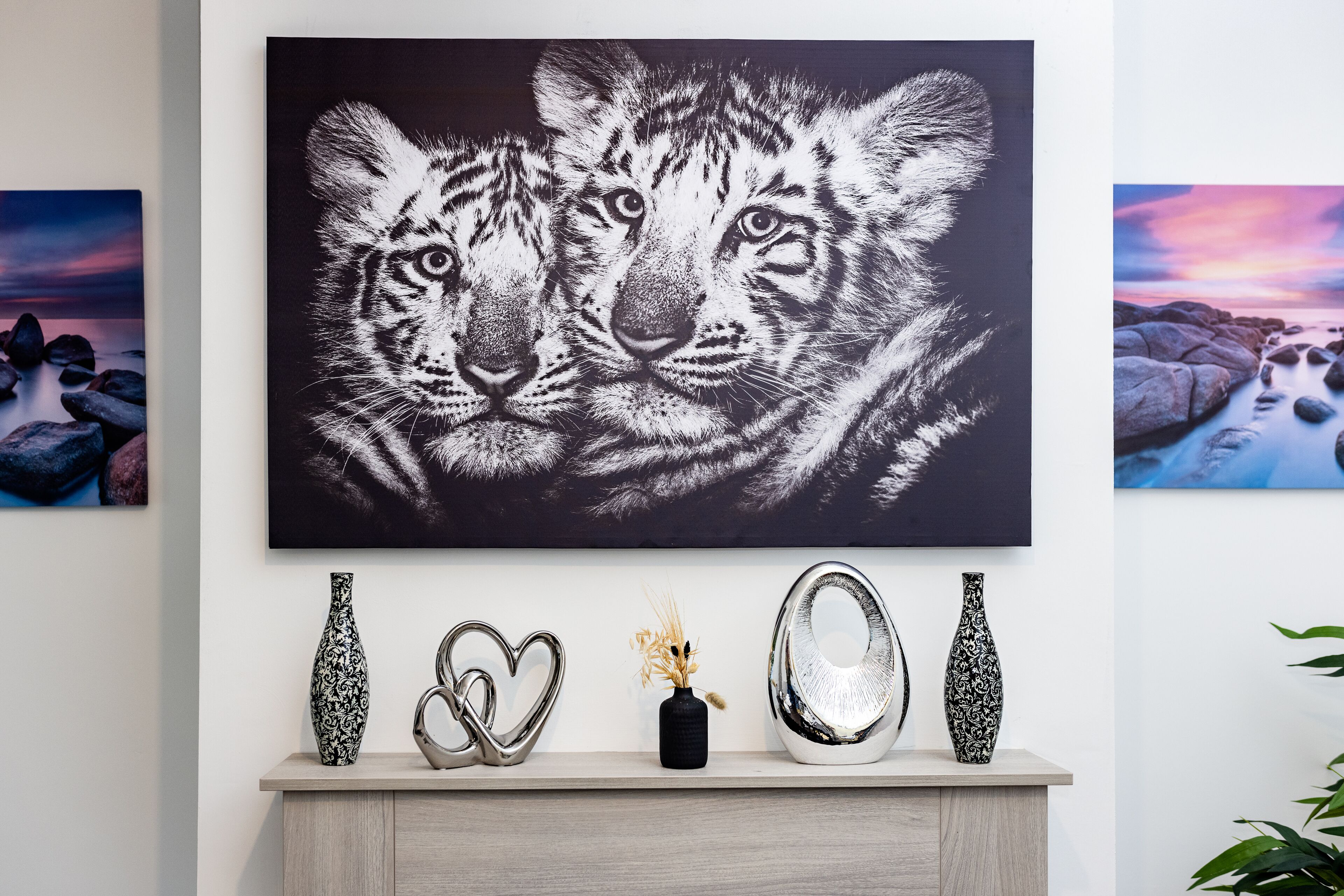 Una pared con un cuadro grande de un tigre, una estantería con jarrones decorativos y una escultura metálica con forma de corazón.