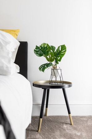 Une chambre à coucher moderne avec un lit, une table de chevet agrémentée d’une plante en pot et une tête de lit noire.