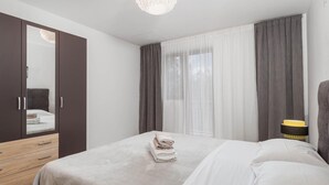 Een slaapkamer met een bed, een kledingkast, een spiegel, een raam met gordijnen en een nachtkastje met een lamp.