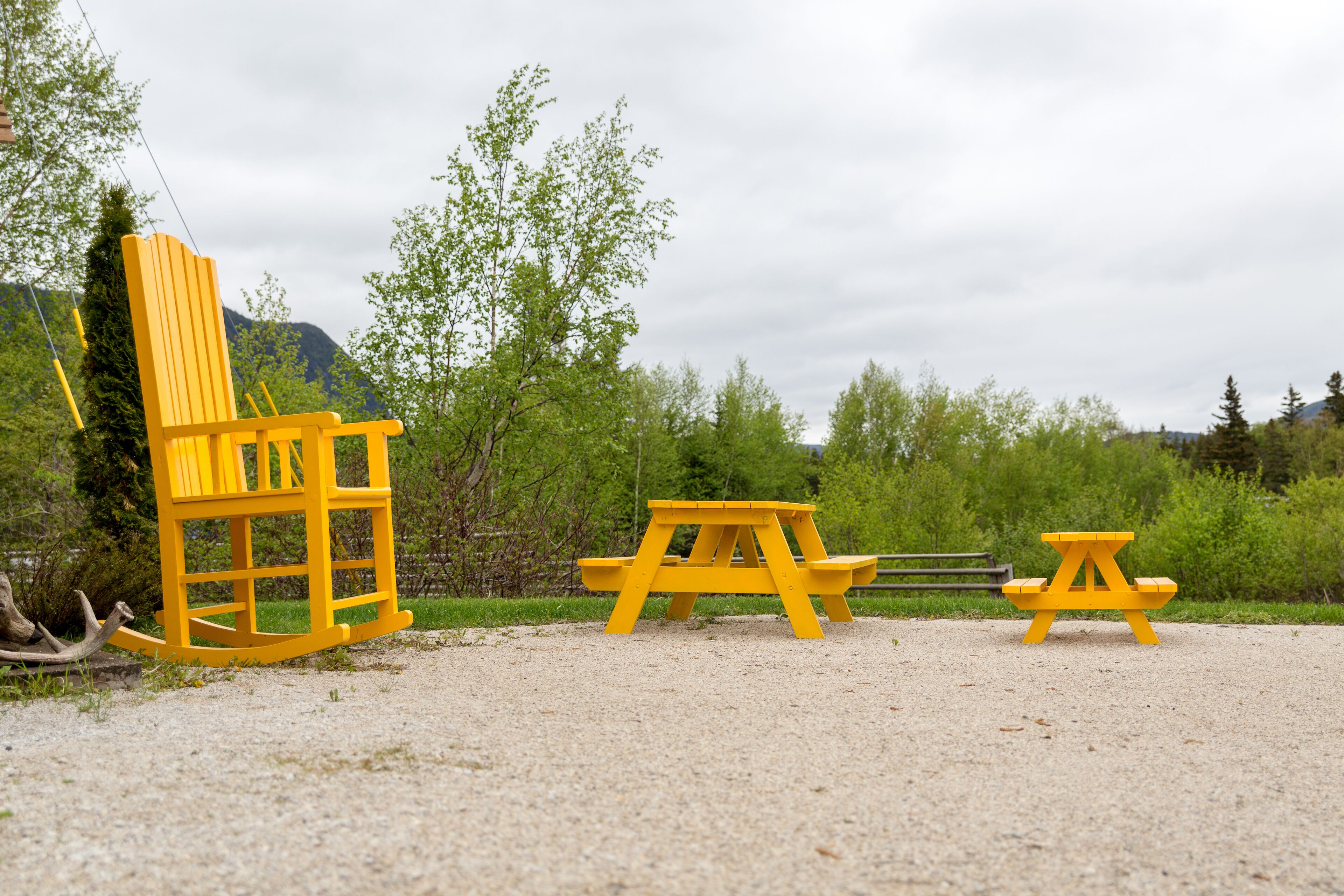 Een picknickopstelling met een gele stoel en twee picknicktafels in een natuurlijke omgeving.