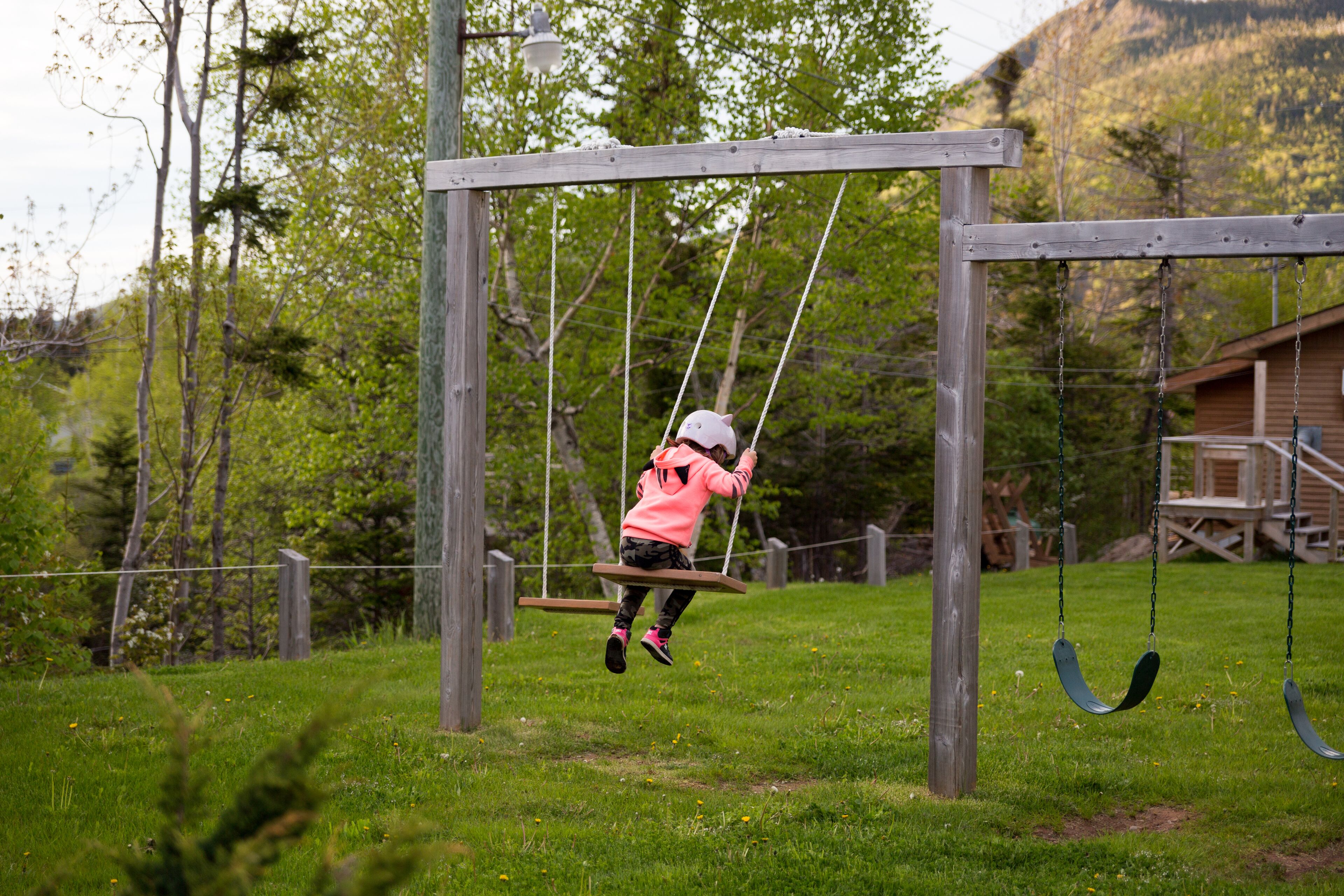 A wooden swing set in a grassy area with trees and a cabin in the background.