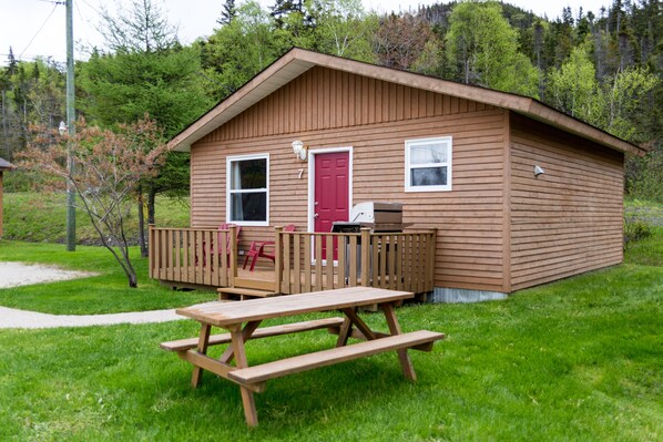 A wooden cabin with a red door, a deck, and a picnic table. - Middle Brook Cottages & Chalets (Glenburnie-Birchy Head-Shoal Brook)