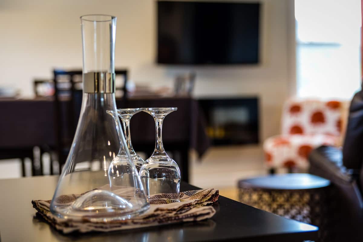 A clear glass decanter and two wine glasses on a table with a placemat.