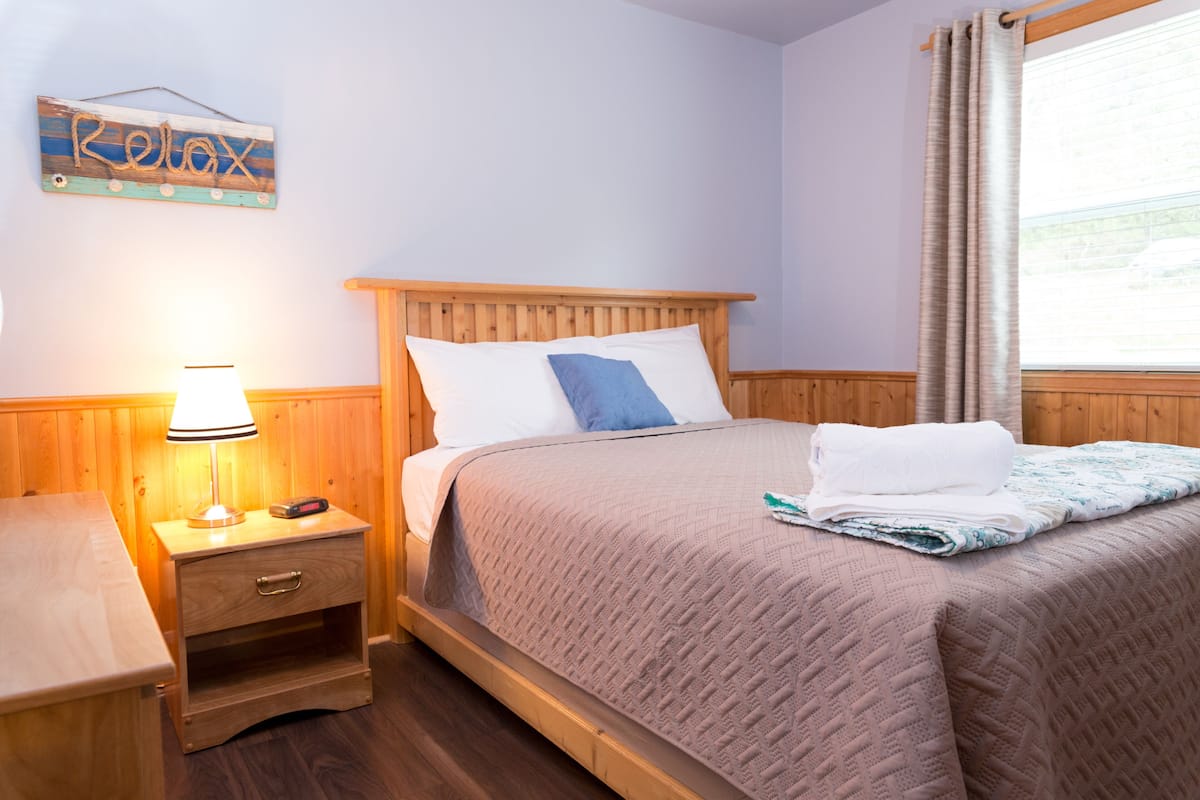 A neatly made bed with a wooden headboard, a bedside table with a lamp, and a 'Relax' sign on the wall.