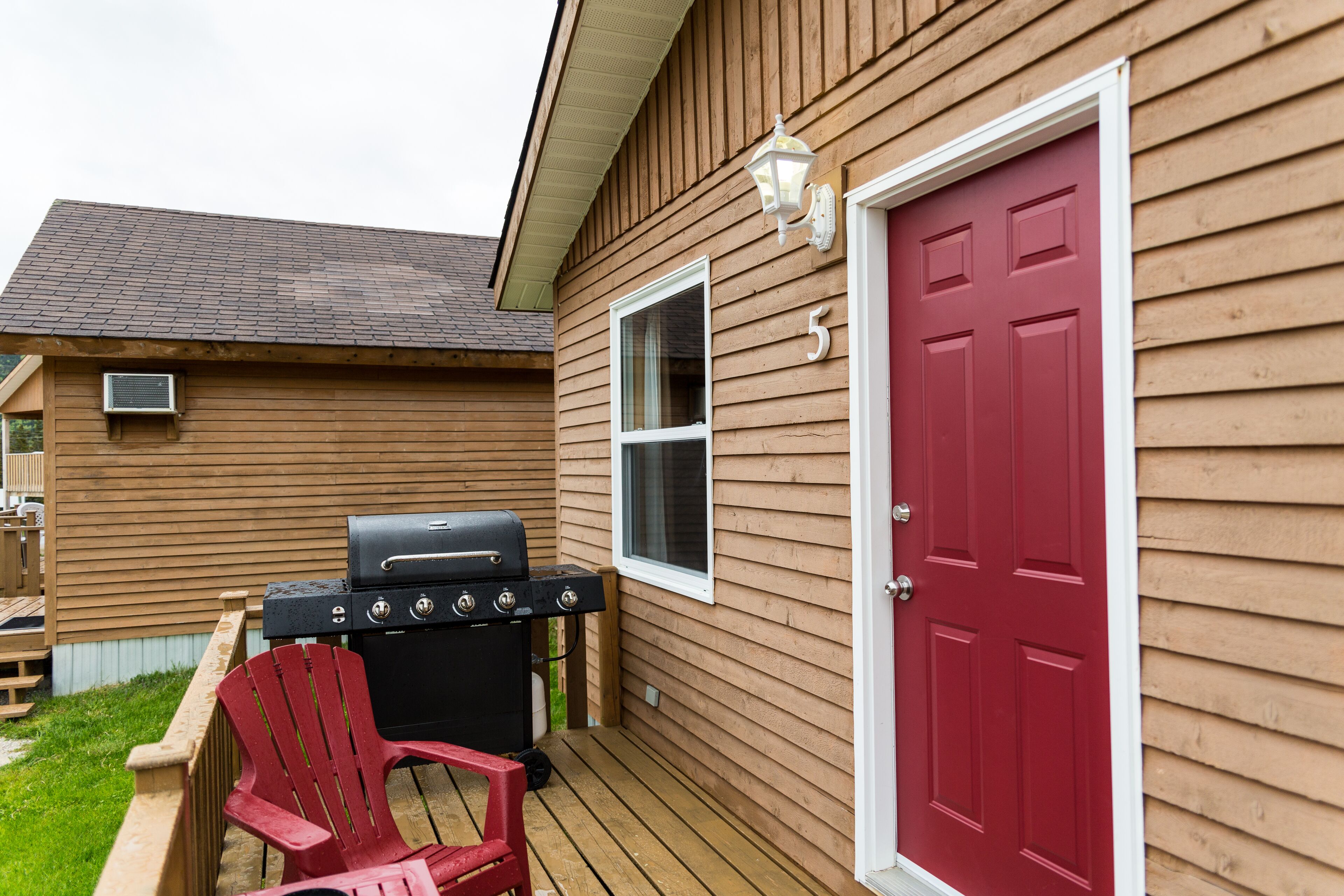 A wooden house with a red door, a grill, and a red chair on the porch.