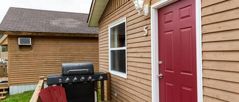 A wooden house with a red door, a grill, and a red chair on the porch.