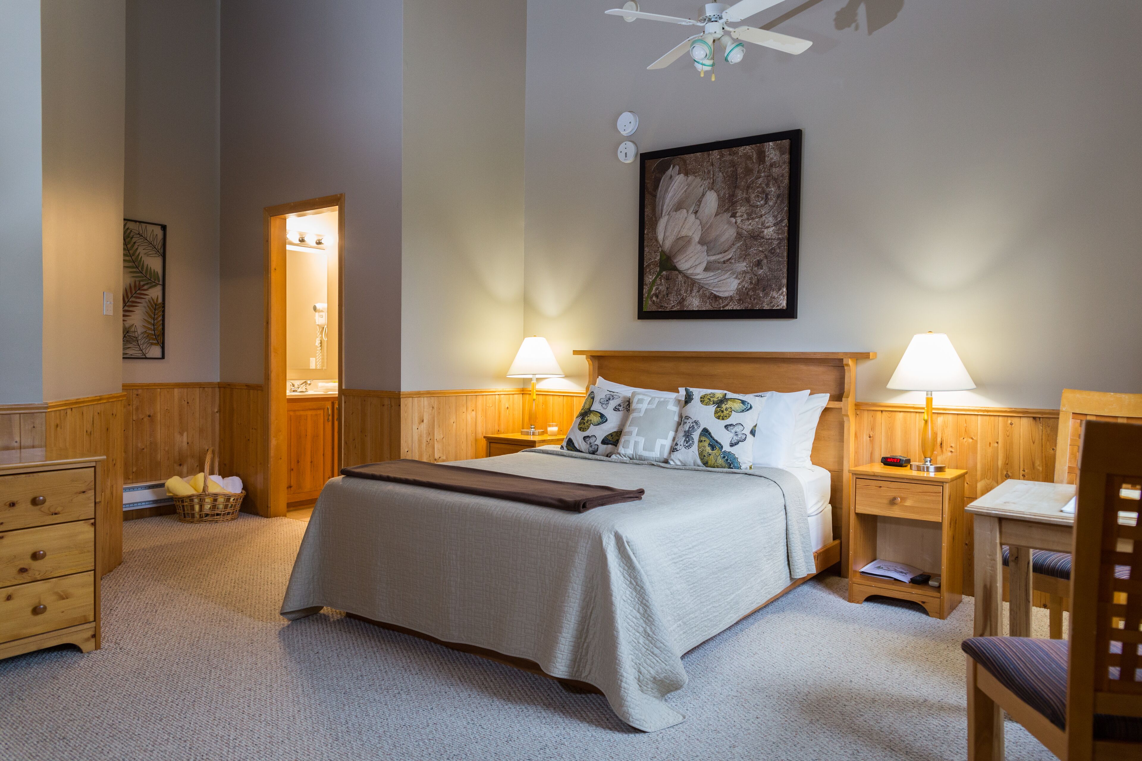 A neatly arranged bedroom with a bed, two bedside tables with lamps, a wooden dresser, and a ceiling fan.