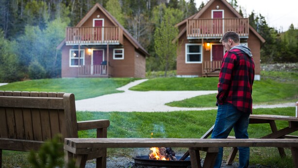 A wooden cabin with a balcony, surrounded by a grassy area and a forest. - Middle Brook Cottages & Chalets (Glenburnie-Birchy Head-Shoal Brook)