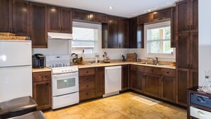 A modern kitchen with dark wooden cabinets, white appliances, and a tiled floor. - Middle Brook Cottages & Chalets (Glenburnie-Birchy Head-Shoal Brook)