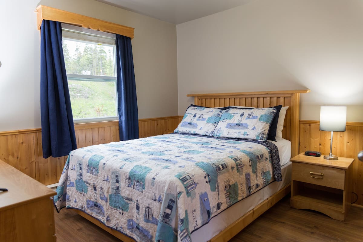 A bedroom with a wooden bed, a nightstand with a lamp, and a window with curtains.