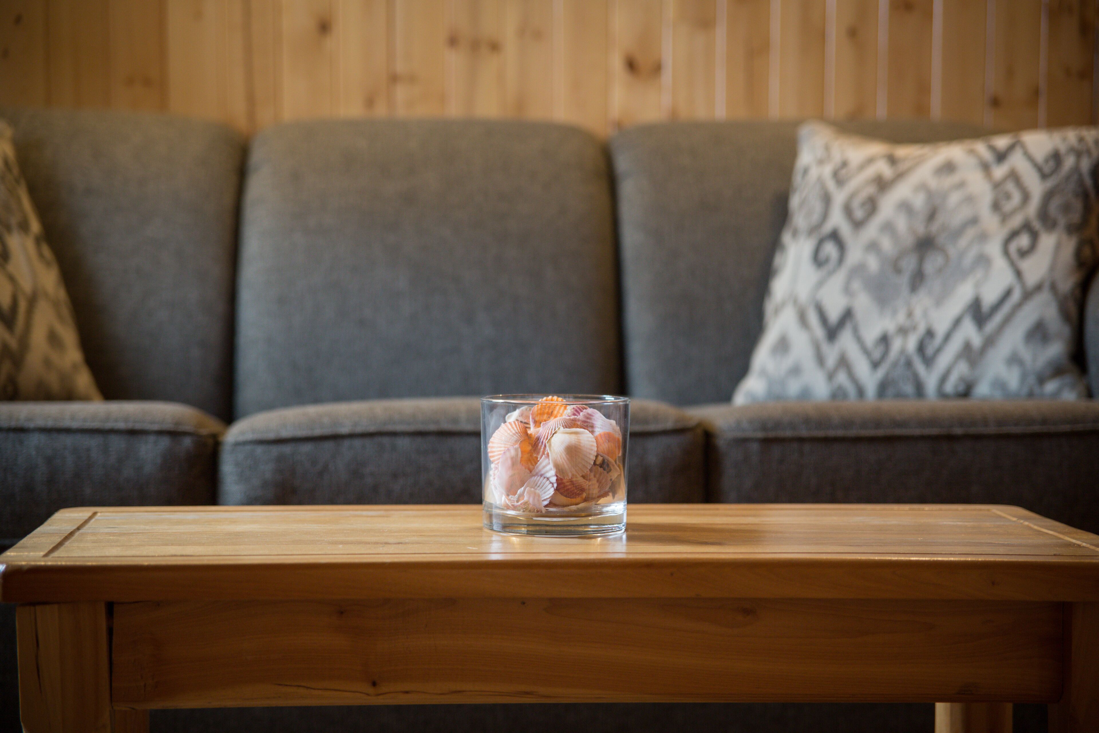 Un recipiente de vidrio con caracoles sobre una mesa de madera frente a un sofá gris con cojines estampados.