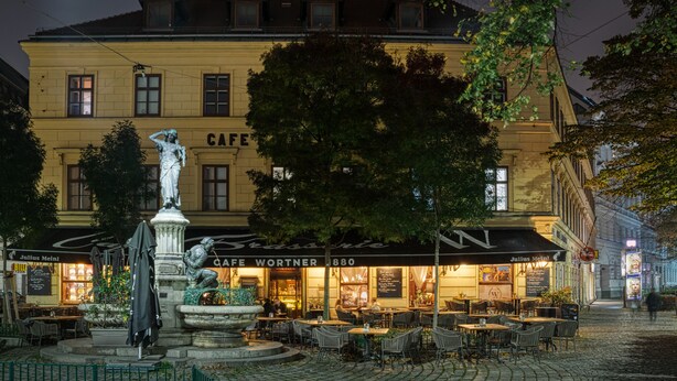 Ett kafé med uteservering, en staty och en byggnad med en skylt som visar texten "CAFE WORTNER 1880".