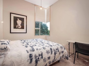A bedroom with a bed, a framed artwork, a window, and a desk.