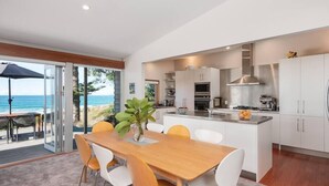 A modern kitchen with white cabinets, stainless steel appliances, and a view of the ocean. - Oceanbeach Escape - Mount Maunganui (Mount Maunganui)