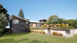 A modern two-story house with a well-maintained lawn and a variety of shrubs and plants. - Oceanbeach Escape - Mount Maunganui (Mount Maunganui)