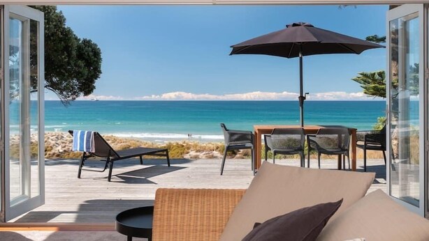 A modern outdoor seating area with a view of the ocean, featuring a table, chairs, and an umbrella. - Oceanbeach Escape - Mount Maunganui (Mount Maunganui)