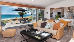 A modern living room with a large glass door leading to a balcony overlooking the ocean. - Oceanbeach Escape - Mount Maunganui (Mount Maunganui)