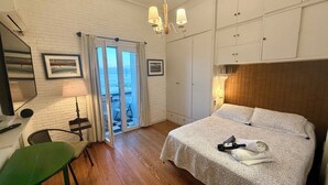 Habitación de hotel con cama, una silla, un escritorio con lámpara, armario y vista al mar a través de un ventanal.
