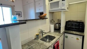 Una cocina compacta con encimera de granito, pileta integrada, microondas, tostadora y refrigerador pequeño.