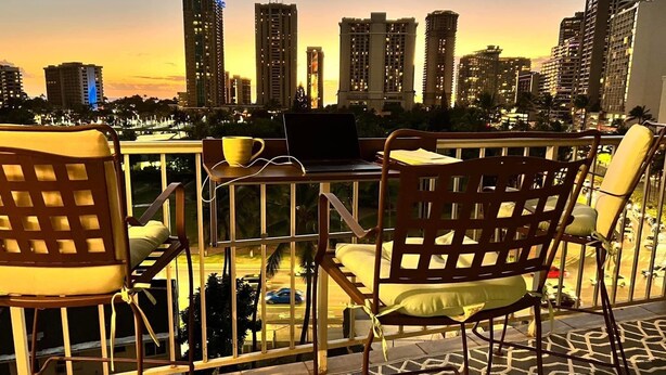 Terraço com mesa e cadeiras, vista para o horizonte da cidade ao pôr do sol.