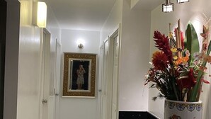 Um corredor com paredes brancas, bancada preta e um vaso com flores.