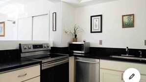 Cozinha moderna com forno embutido, micro-ondas e máquina de lavar louça. Há quadros nas paredes e um vaso de planta no balcão.