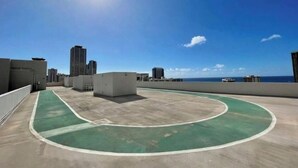 Terraço com quadra esportiva verde, cercado por edifícios e céu claro.