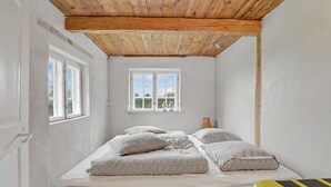 Una habitación con una cama, dos ventanas, techo de madera y vistas al exterior.