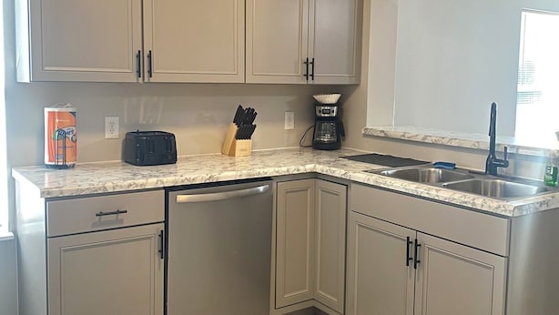 A modern kitchen with light wood cabinets, a built-in dishwasher, a coffee maker, and a sink. - Large group & couples retreat (Pineville)