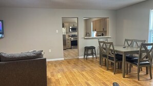 A modern living room with a gray sofa, wooden flooring, and a dining area with a table and chairs. - Large group & couples retreat (Pineville)