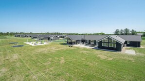 A row of modern, single-story buildings with large windows and a flat roof, surrounded by a well-maintained lawn and a clear sky. - Nice home in Nørre Nebel with sauna (Nørre Nebel)