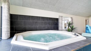 A modern bathroom with a large bathtub, dark tiled walls, and a window with curtains. - Nice home in Nørre Nebel with sauna (Nørre Nebel)