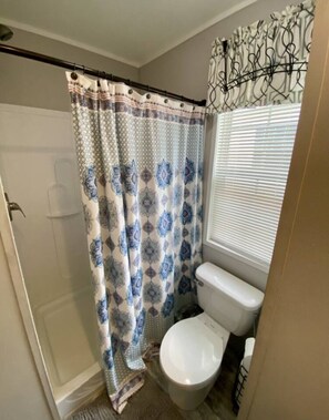 A bathroom with a shower curtain, toilet, and a window with blinds. - Rainbow River Bungalow T (Dunnellon)