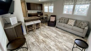 Un espai habitable reduït amb una cuineta, un sofà, una zona de menjador i un televisor fixat a la paret.
