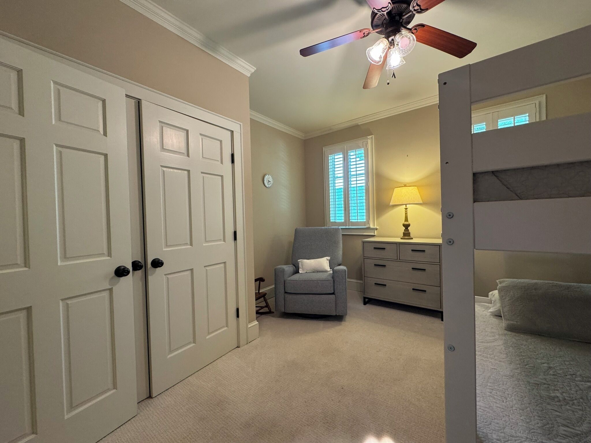 A bedroom with a bunk bed, a desk with a lamp, a chair, and a window with blinds.