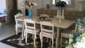 Un'area pranzo con un tavolo grande, sedie bianche, un vaso azzurro con fiori e uno specchio sopra il tavolo.