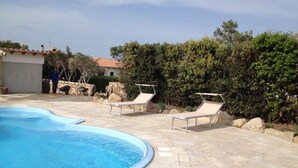 Una piscina con lettini, un patio in pietra e una persona sullo sfondo.