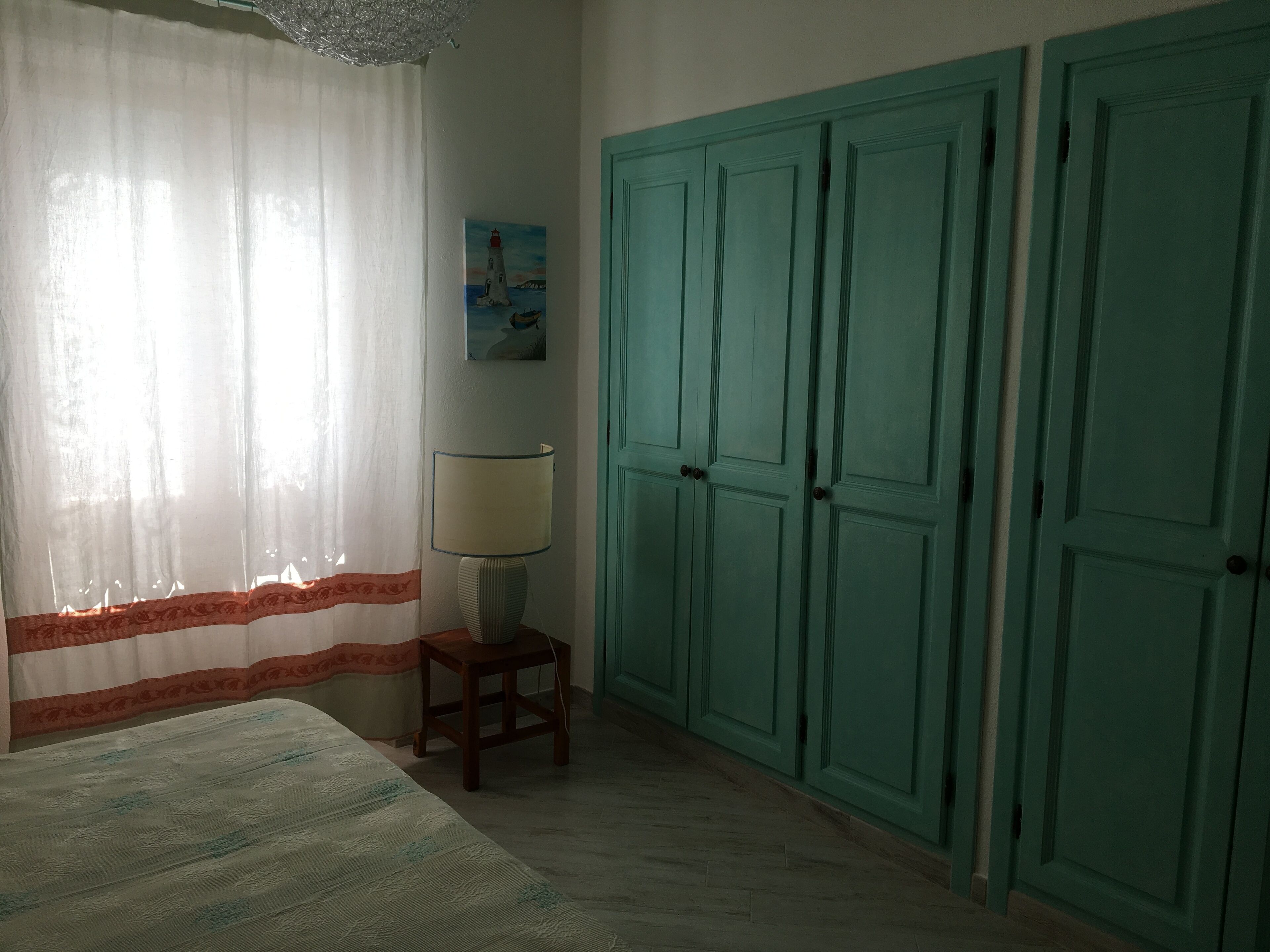 A bedroom with a bed, a lamp, a painting, and a set of green wardrobes.