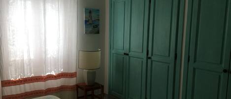A bedroom with a bed, a lamp, a painting, and a set of green wardrobes.