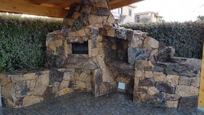 Un'area cucina esterna in pietra con forno integrato e una panca.