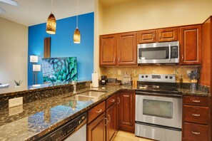 Una cocina moderna con encimeras de granito, electrodomésticos de acero inoxidable, armarios de madera y una pared de acento azul.