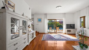A spacious living room with wooden flooring, a large cabinet, a television, and a sliding glass door leading to an outdoor area. - Luxurious home in Vodice (Vodice)