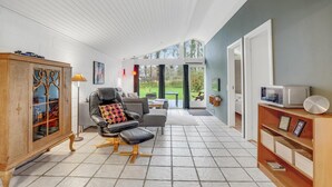 A spacious living area with a leather armchair, a wooden cabinet, and a television on a wooden shelf.