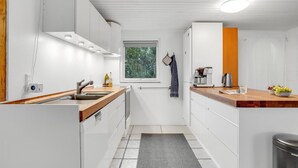 A compact kitchen with white cabinetry, a wooden countertop, a built-in oven, and a window with a view of trees.