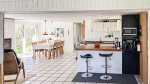 A modern kitchen with a dining area, featuring a central island with bar stools, wooden cabinets, and a microwave.