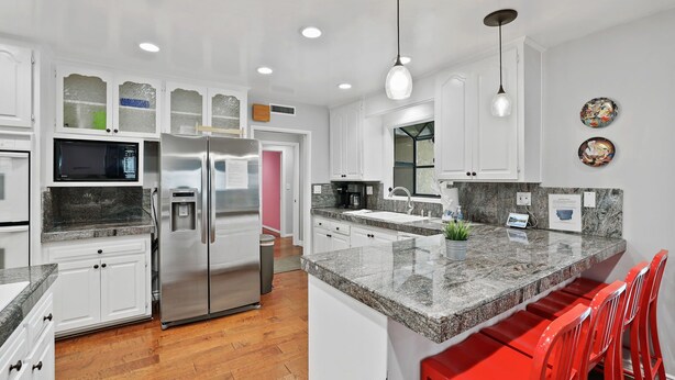 Una cocina moderna con gabinetes blancos, electrodomésticos de acero inoxidable, encimeras de granito y taburetes de bar rojos.