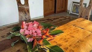 Une table à manger en bois agrémentée d’un centre de table floral, des chaises en bois dont les dossiers sont ajourés, et une porte en bois visible au fond.