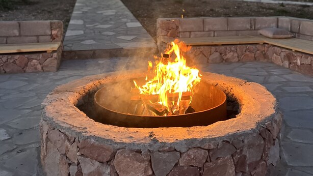 A stone fire pit with a fire burning in the center, surrounded by a stone wall. - Green Villa Resort Blue (dilijan)