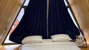 A cozy, sloped-roofed room with a bed, pillows, and a window with curtains. - Green Villa Resort Blue (dilijan)