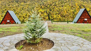 A building with a triangular roof and a brick facade, surrounded by a stone pathway and a small evergreen tree. - Green Villa Resort Blue (dilijan)